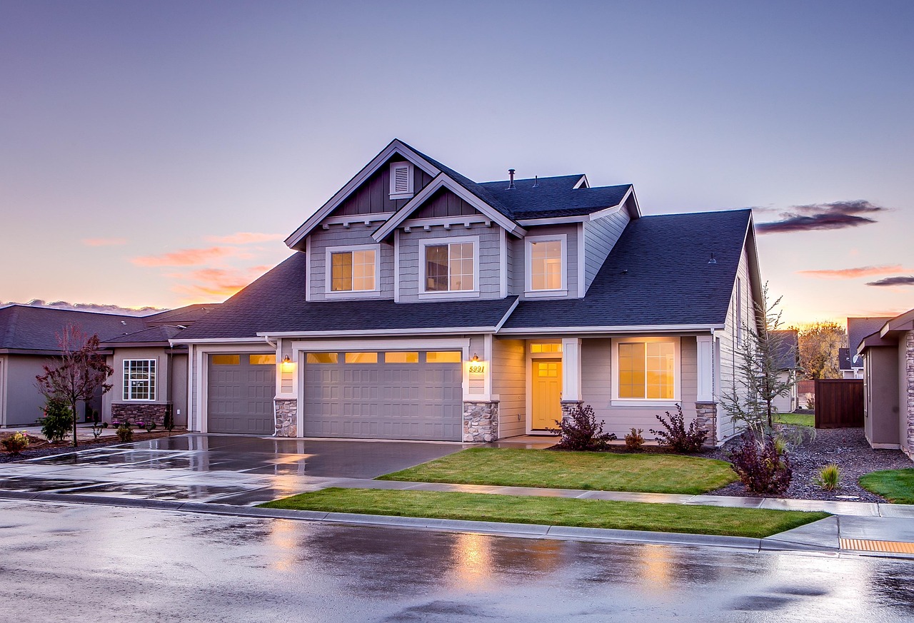 A two-story house with gray siding at dusk, lights on