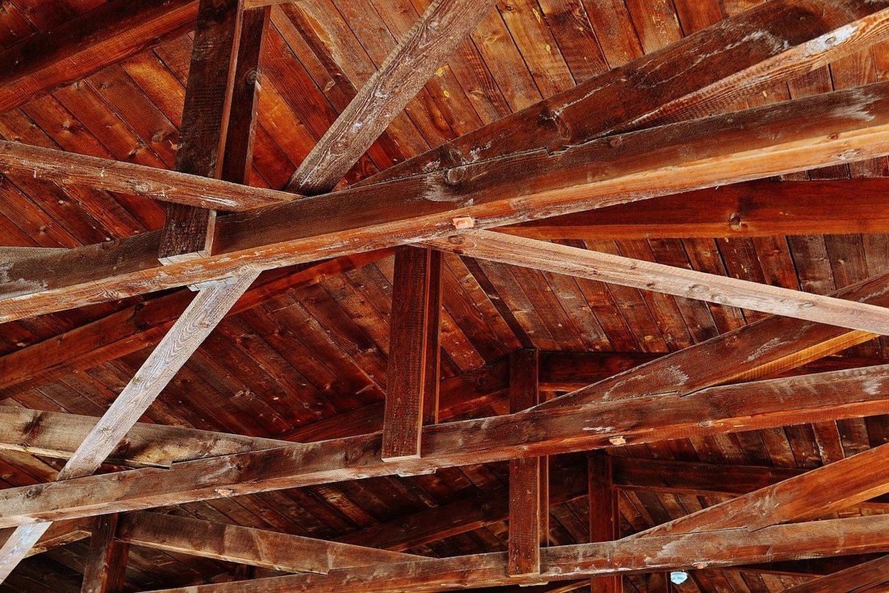 Wooden roof beams and trusses in a rustic, aged structure.