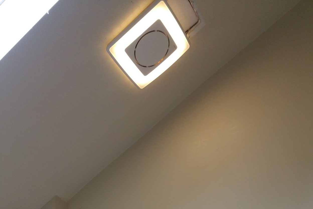 A square LED bathroom exhaust fan in a ceiling, with a yellow stepladder below it