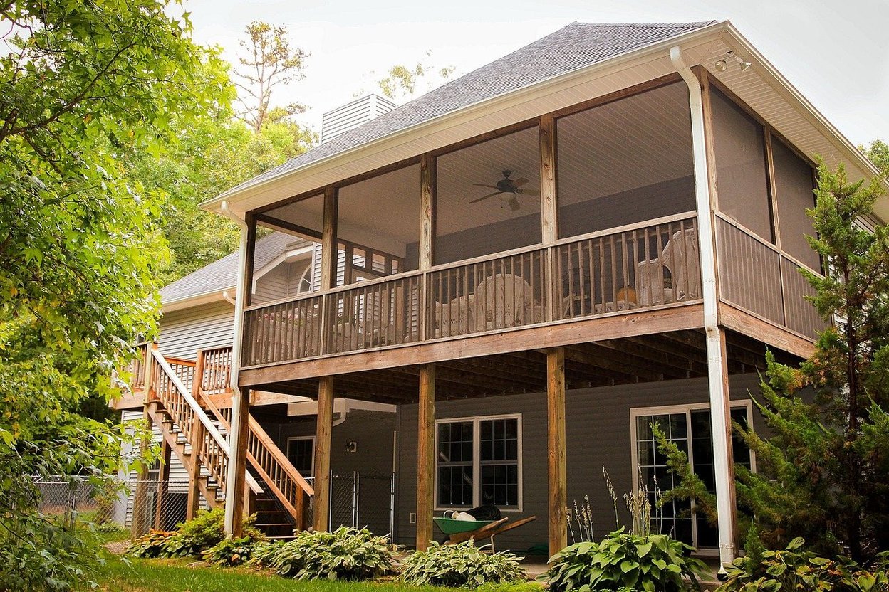 A raised wooden backyard deck with railings and stairs on the back of a house