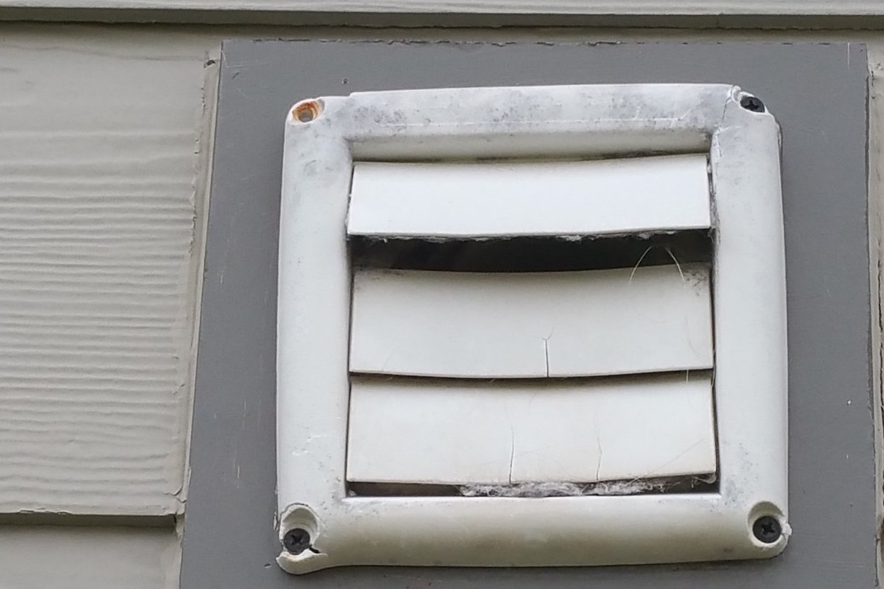 A louvered dryer vent hood on gray vinyl siding