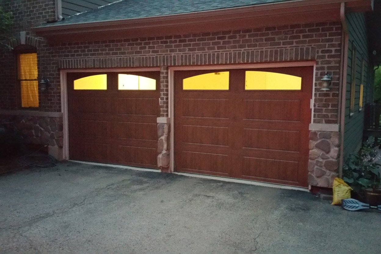A two-car brick garage with new wood-look carriage doors at dusk
