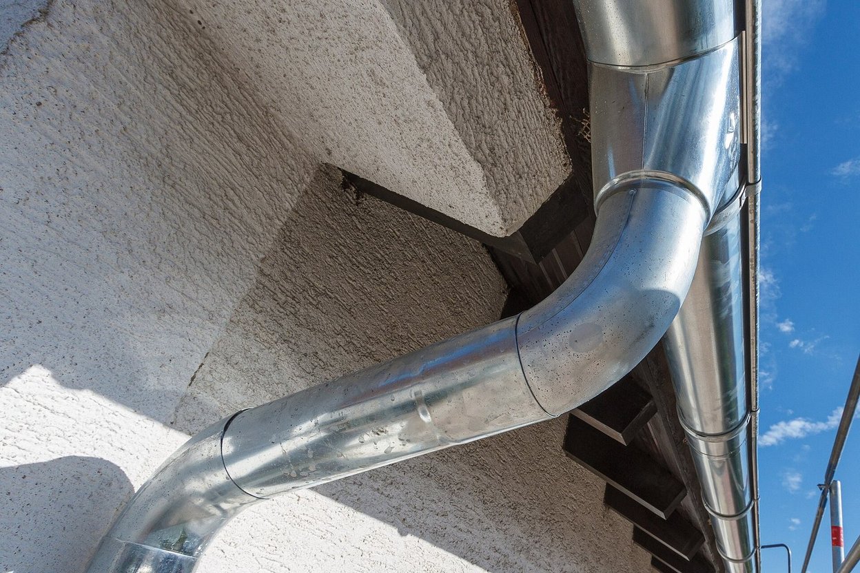 A metal downspout carrying rainwater from a gutter down a wall