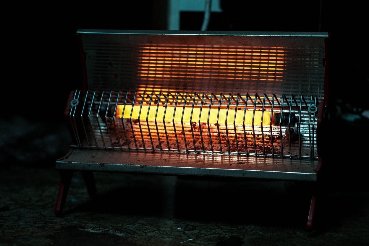 A glowing electric space heater with metal grates and red legs.