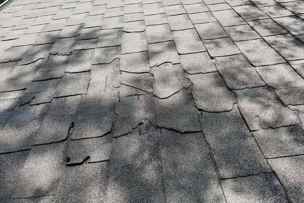Close-up of a weathered asphalt shingle roof with cracked and lifting shingles