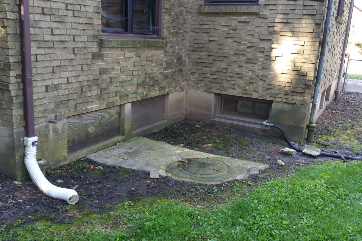 Capped white PVC sewer cleanout pipe rising from a lawn beside a house foundation