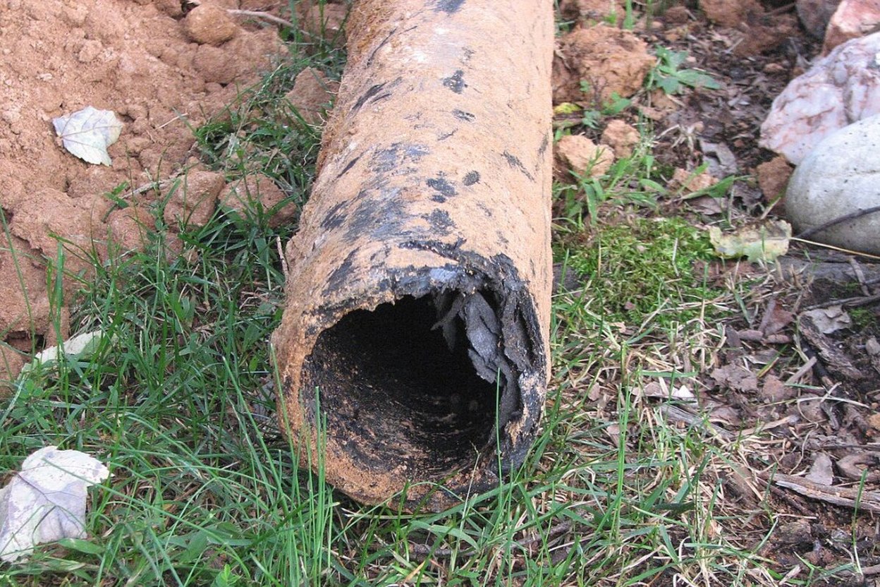 Sewer camera view inside a dark Orangeburg pipe, with a flattened cross-section, a peeling wall layer, and a separated joint.