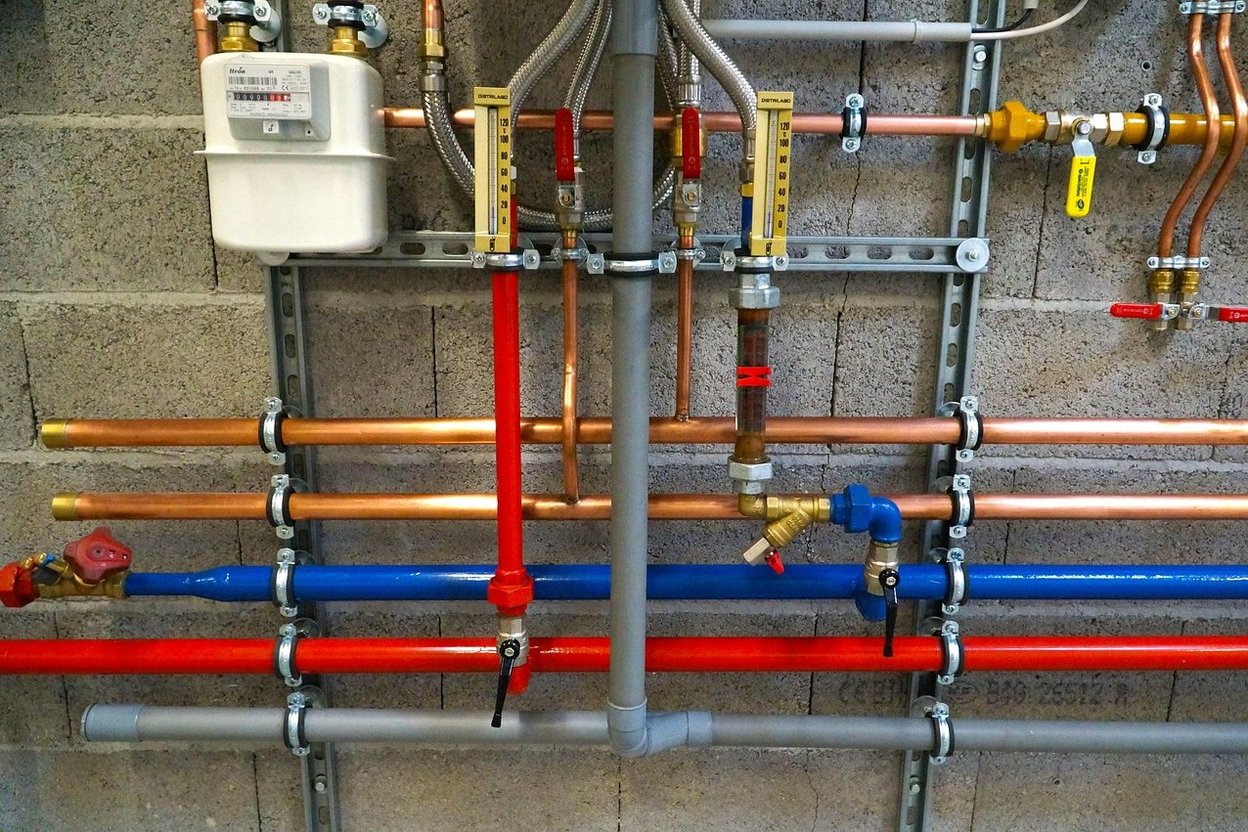 Wall-mounted copper and PVC plumbing with valves, gauges, and color-coded pipes.