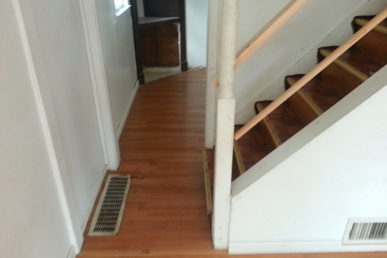 A wooden staircase with a handrail rising beside a hallway with hardwood floors