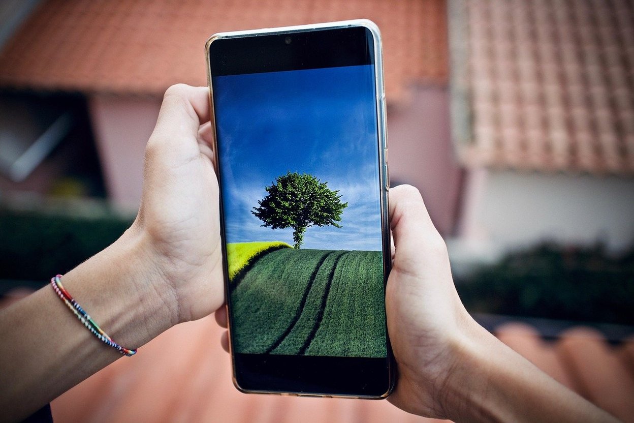 Two hands holding a smartphone up in front of a house