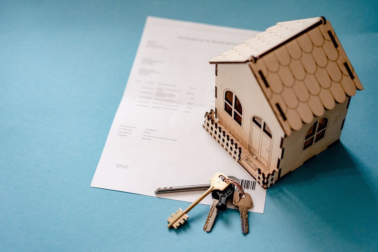 Wooden house model with keys and documents on blue background.
