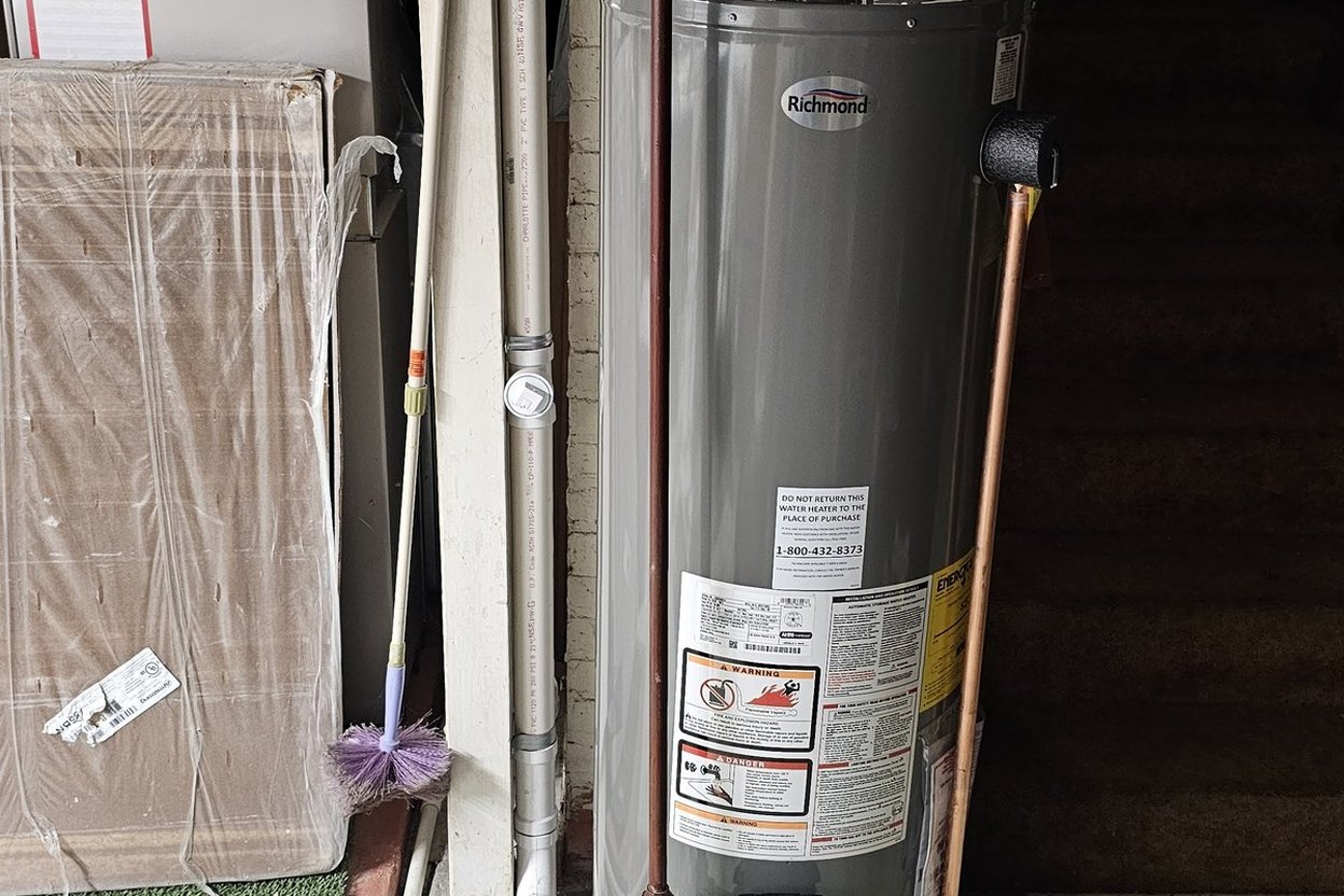 A gas tank water heater with its label and copper relief-valve discharge pipe, next to the house plumbing