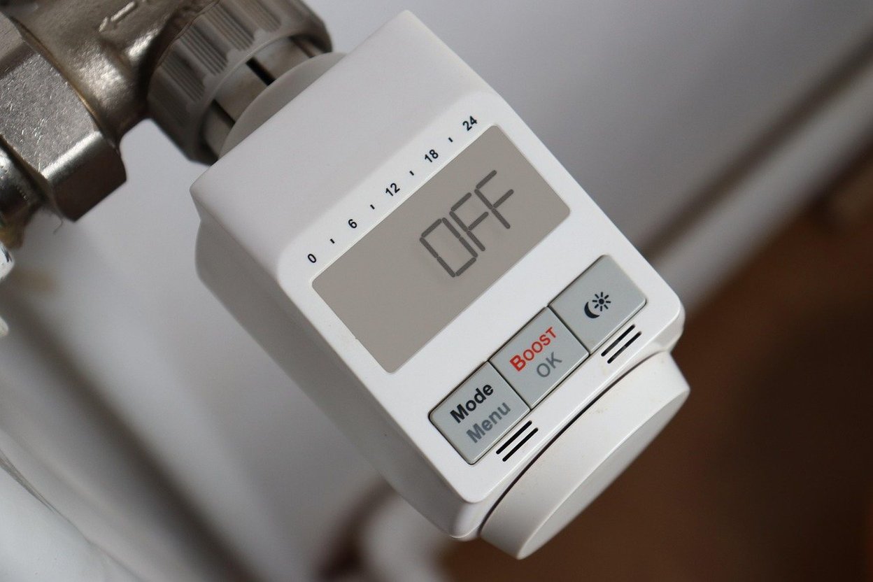 A homeowner's hand adjusting a thermostat in a living room while warm air blows from a floor heating vent.