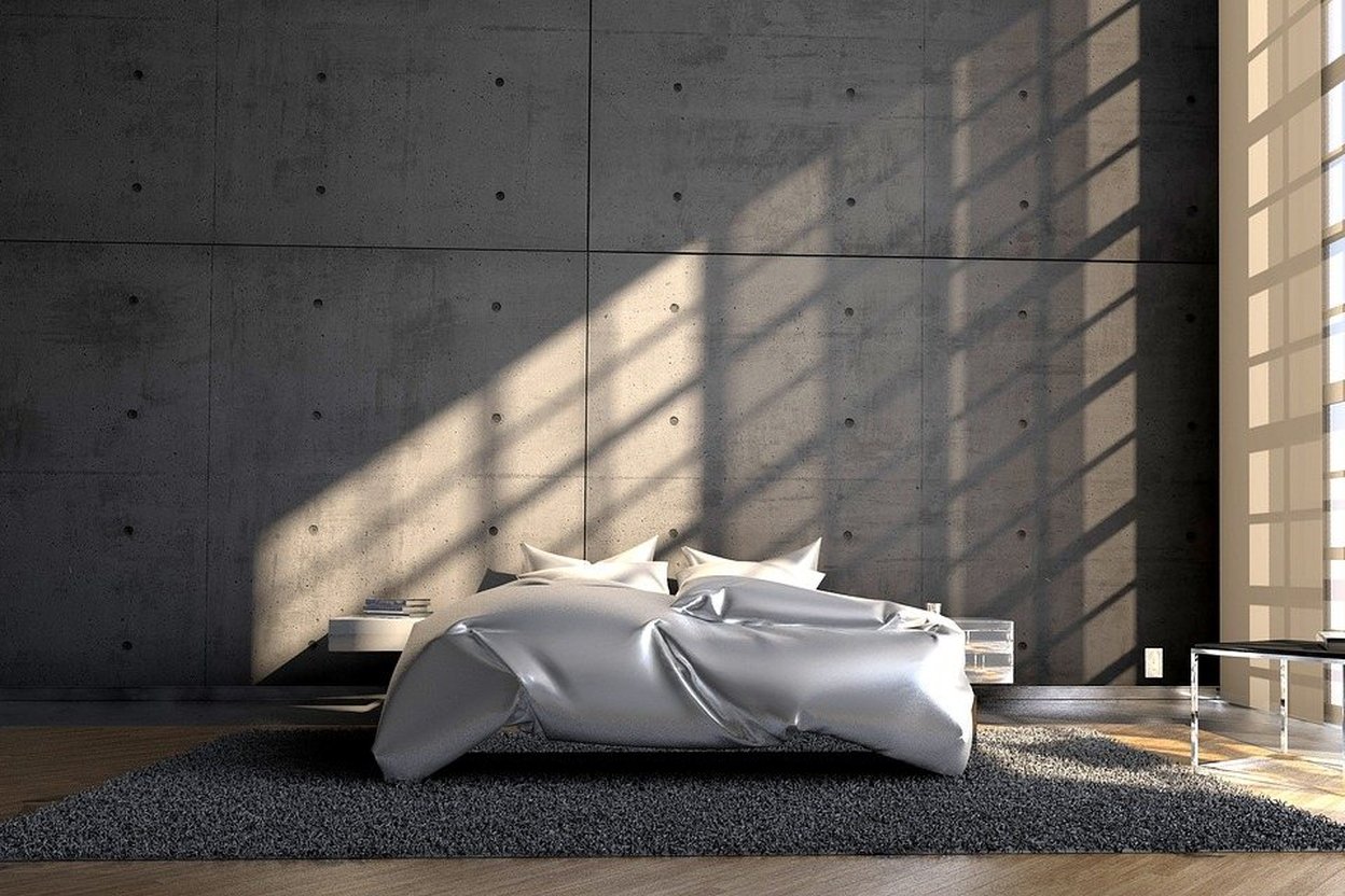 Modern bedroom with concrete walls and sunlight casting shadows on the bed.