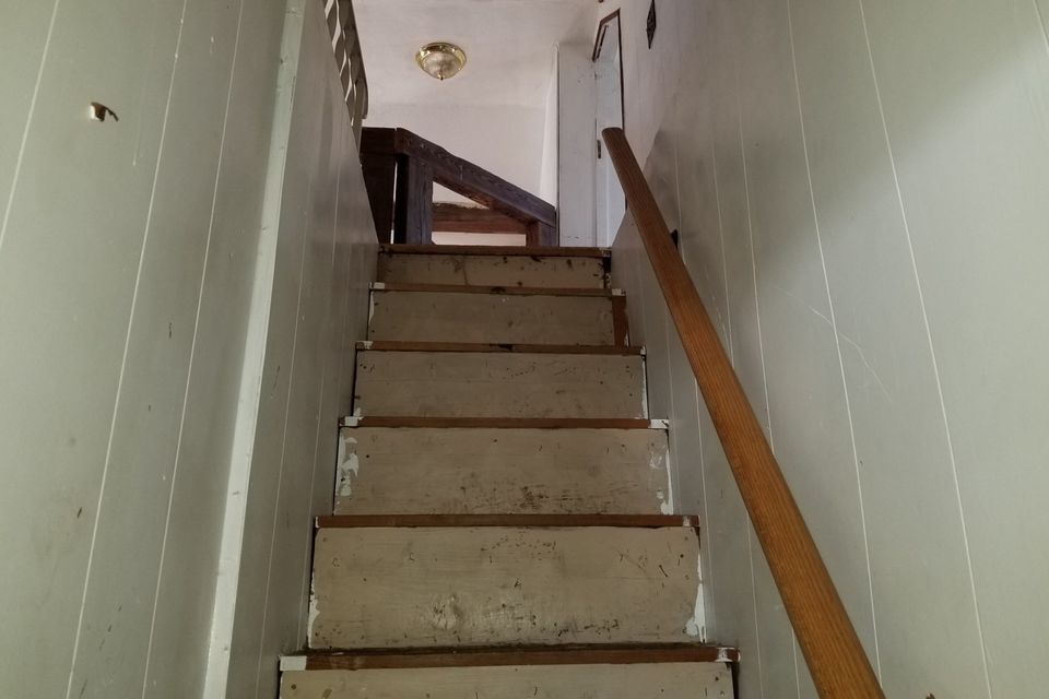 A steep, narrow staircase with bare treads and a wall-mounted handrail