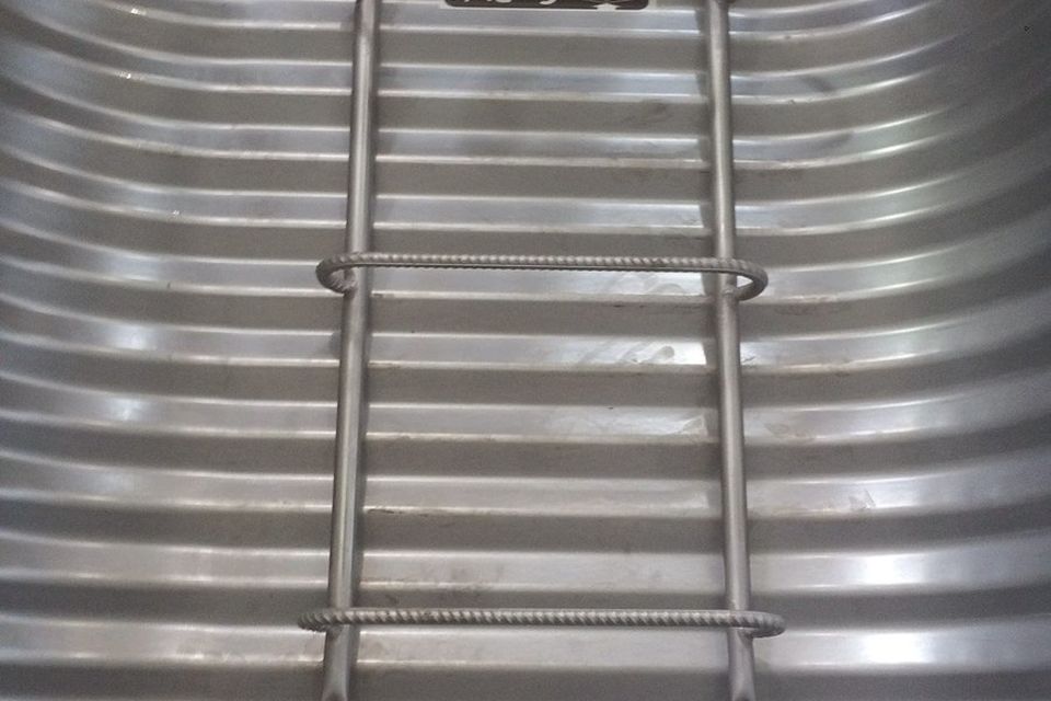 Looking up from inside a deep egress window well with a built-in ladder and a grate cover overhead